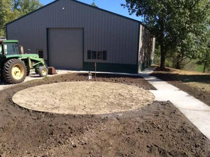 Round stamped concrete pad and walk in front of a dark steel shop building